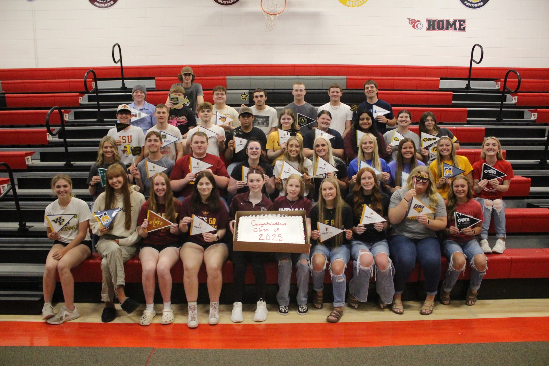 Group photo of the class of 2025 with a graduation cake and pennants representing their plans for life after high school.