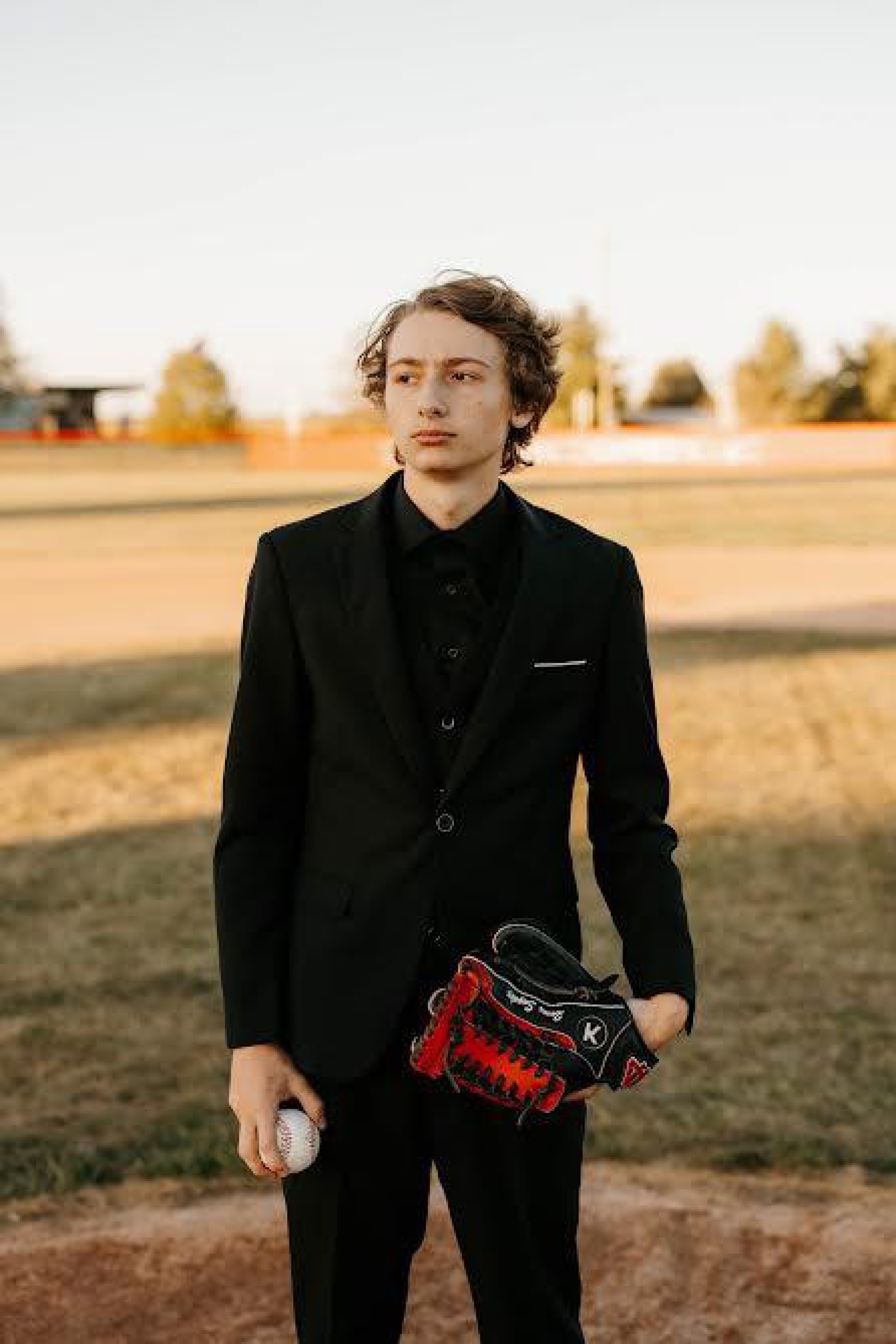 male student posing in field wearing a baseball glove and holding a baseball