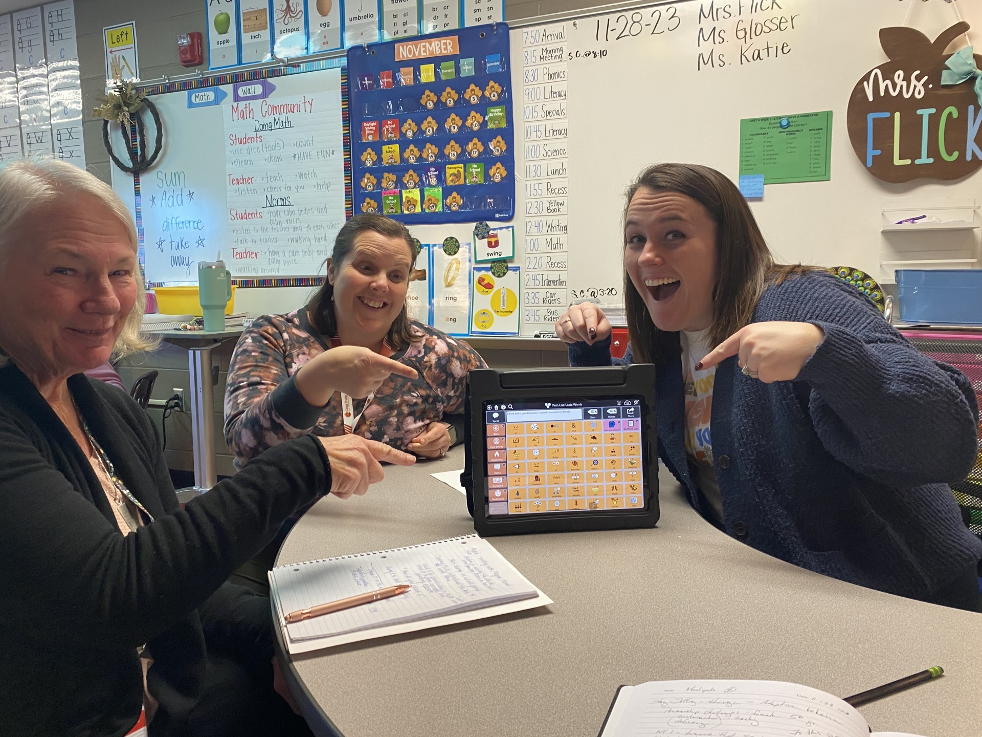 Three Cardinal teachers sitting at a classroom table excitedly pointing at an ipad that is showcasing a speech-based learning tool