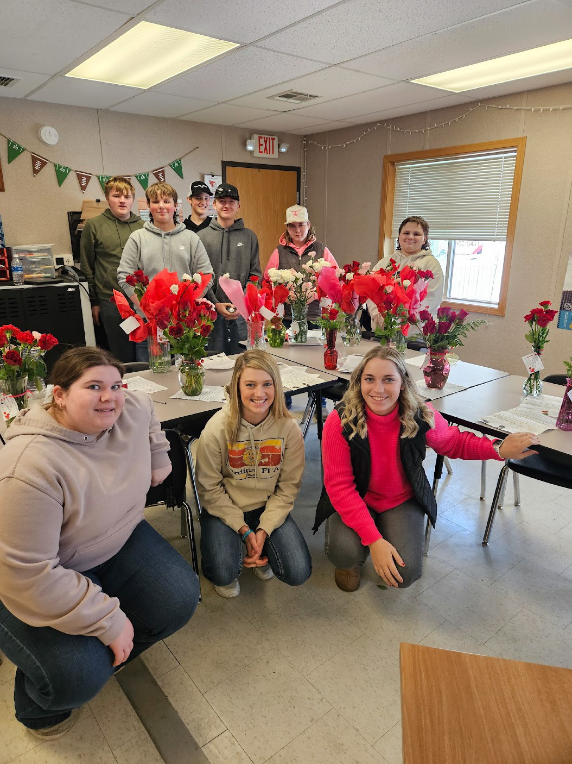 FFA students pose around school tables with red roses in vases on them.
